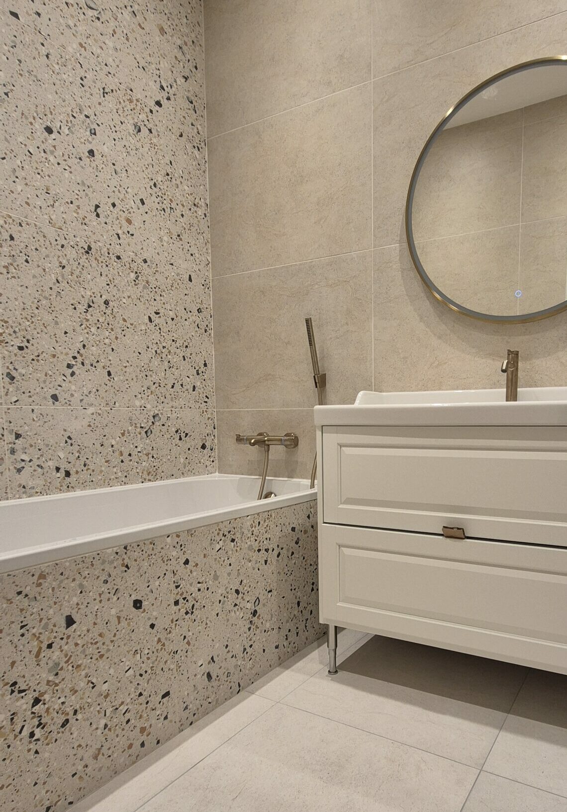 Pose de carrelage Salle de bains avec carrelage effet pierre beige et terrazzo, baignoire intégrée et robinetterie dorée à Lyon