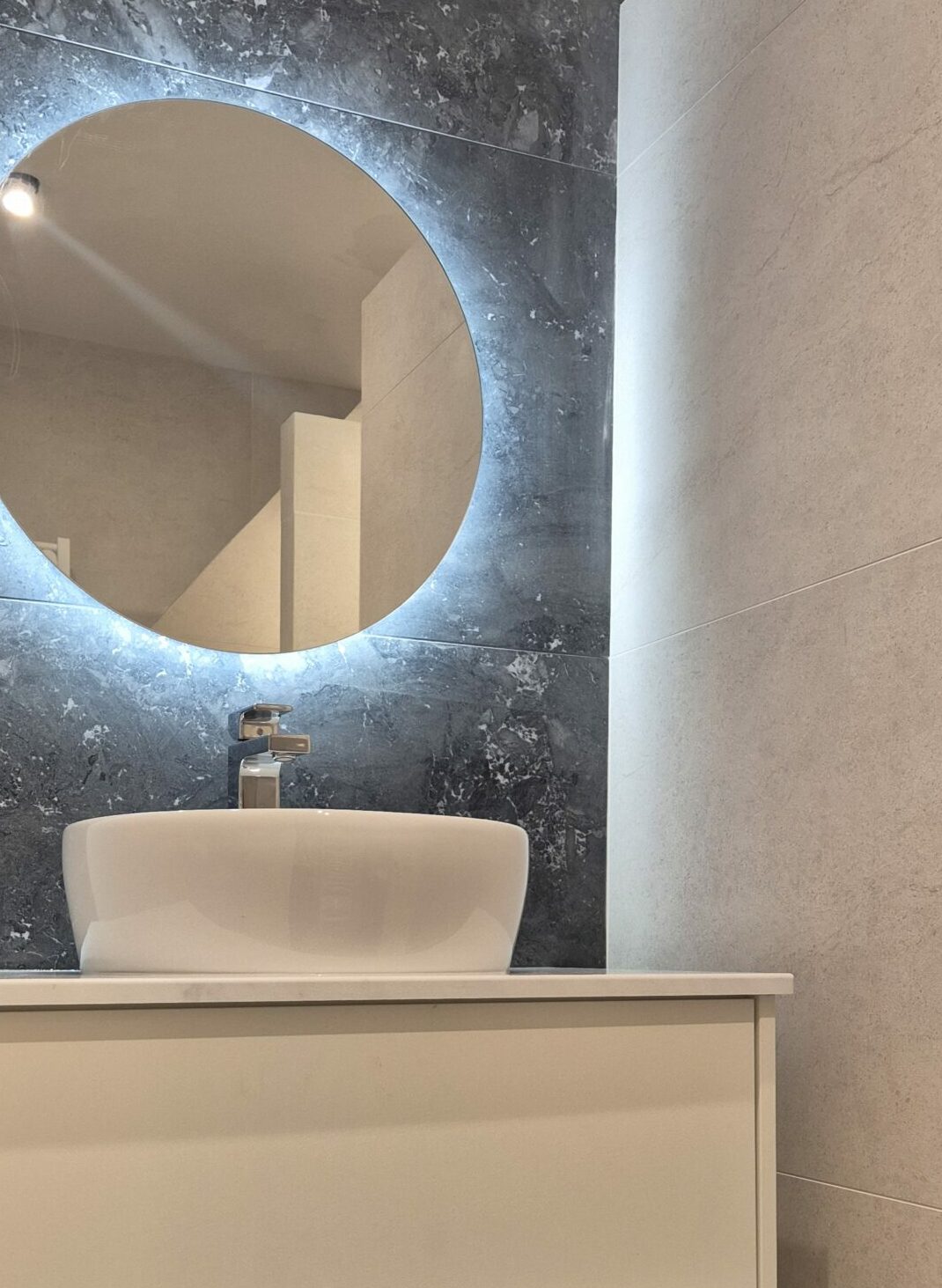 Pose de carrelage Salle de bains moderne avec carrelage effet pierre beige et miroir rétroéclairé sur mur en marbre noir à Lyon