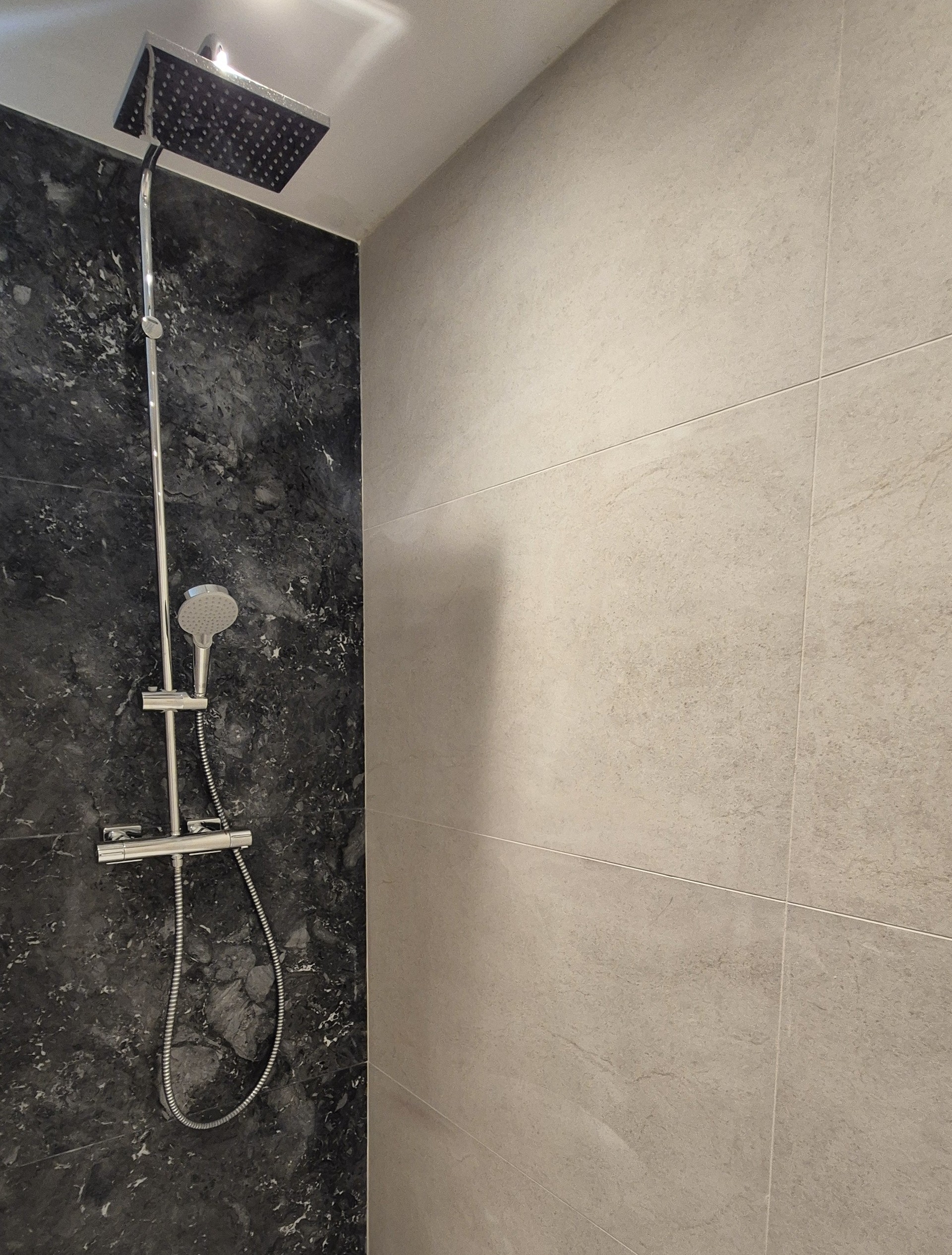 Pose de carrelage Salle de bains moderne avec carrelage effet pierre beige et mur en marbre noir à Lyon