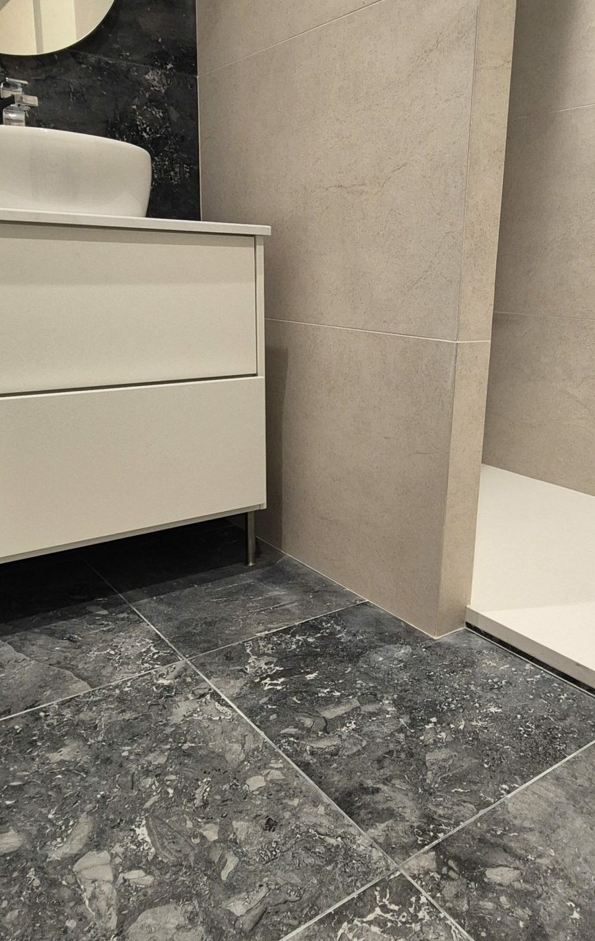 Pose de carrelage Salle de bains moderne avec sol en carrelage effet marbre noir, murs en pierre beige et meuble vasque blanc à Lyon