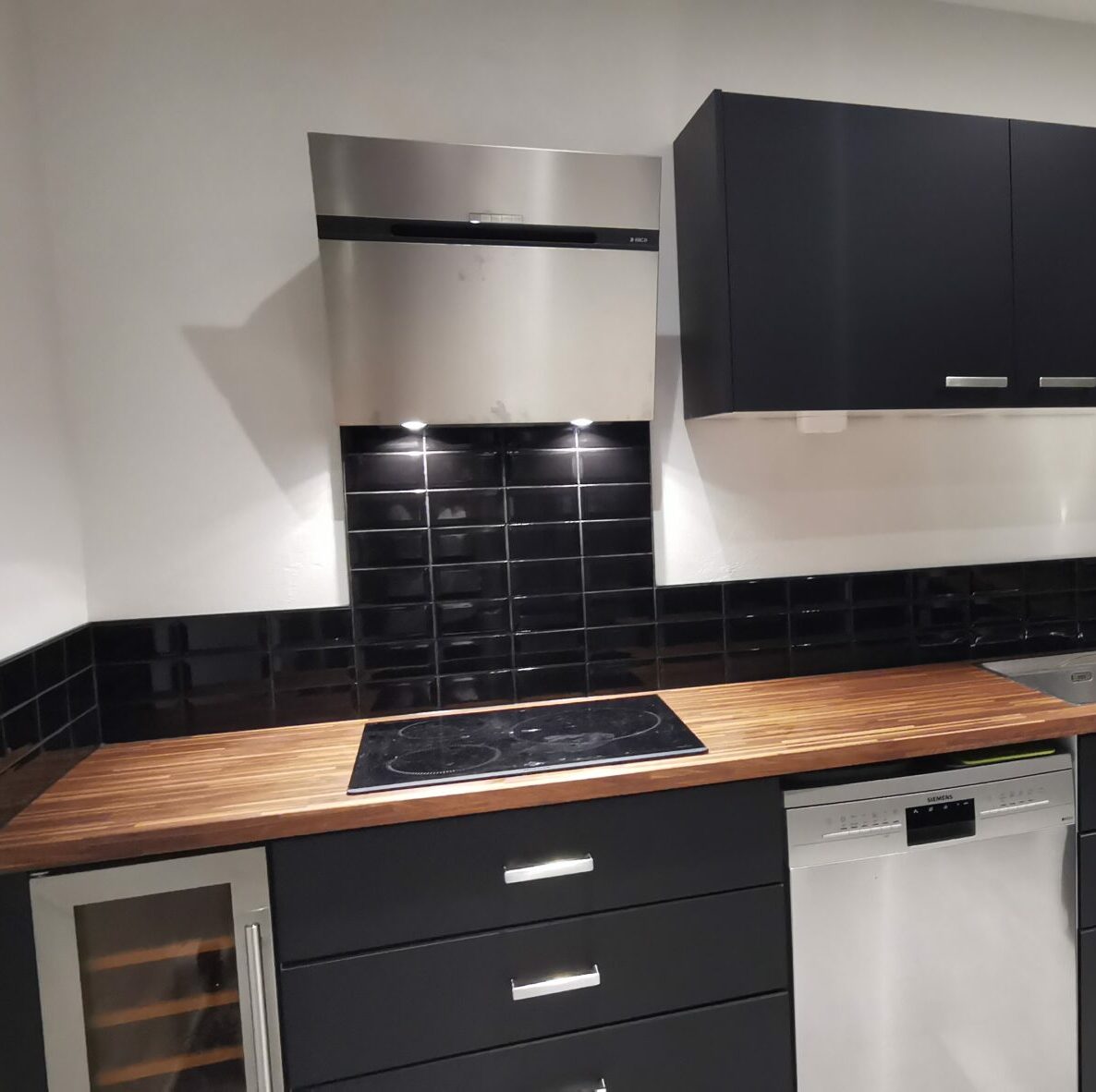 Pose de carrelage Cuisine moderne avec meubles noirs, plan de travail en bois et crédence en carrelage métro noir brillant à Lyon